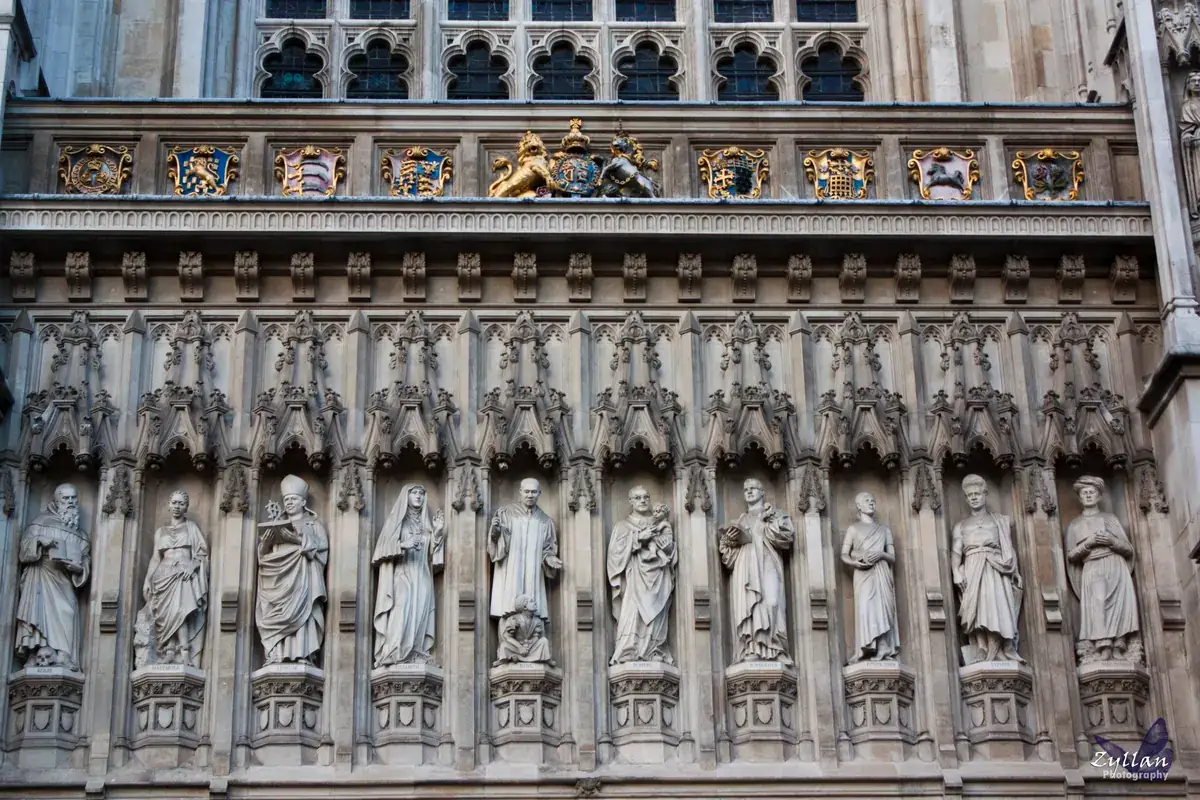Ten carved stone statues of twentieth-century martyrs in niches above the west door of Westminster Abbey, beneath a row of painted coats of arms