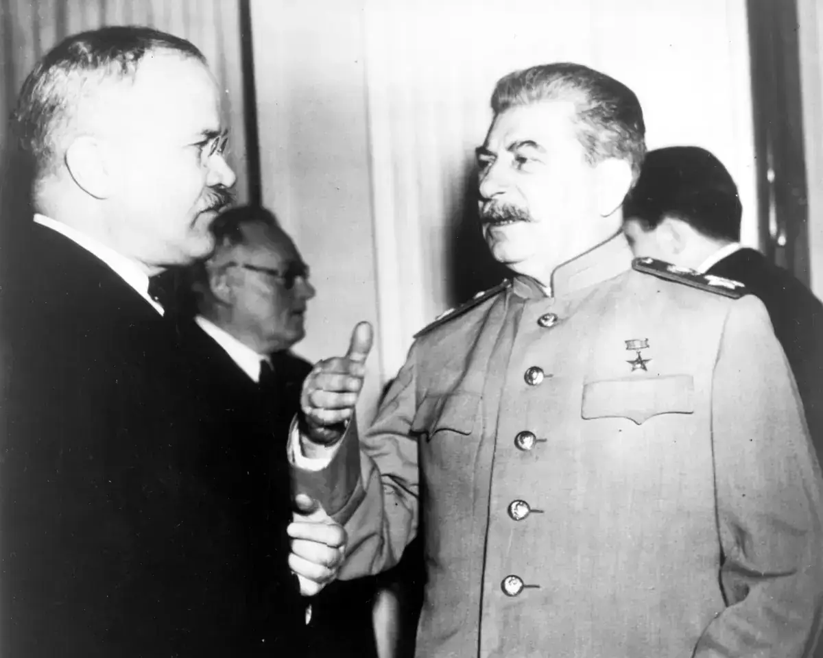 Black-and-white photograph of Joseph Stalin in a pale military tunic with a star medal, gesturing as he talks with Vyacheslav Molotov, who wears glasses and a dark suit