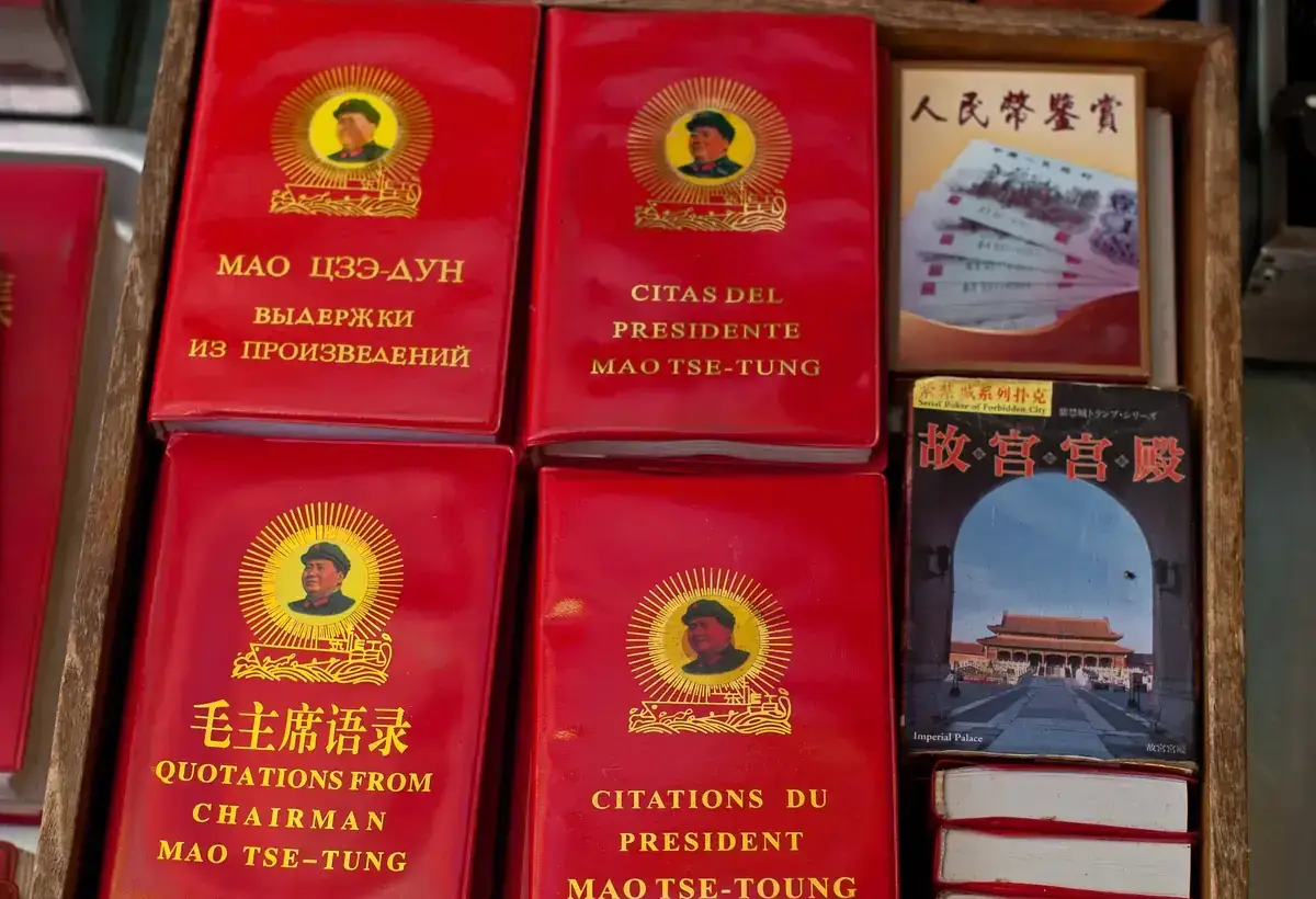 A wooden tray of red plastic-covered copies of Quotations from Chairman Mao, each with Mao's portrait in a gold sunburst, titled in Chinese, English, French, Spanish and Russian