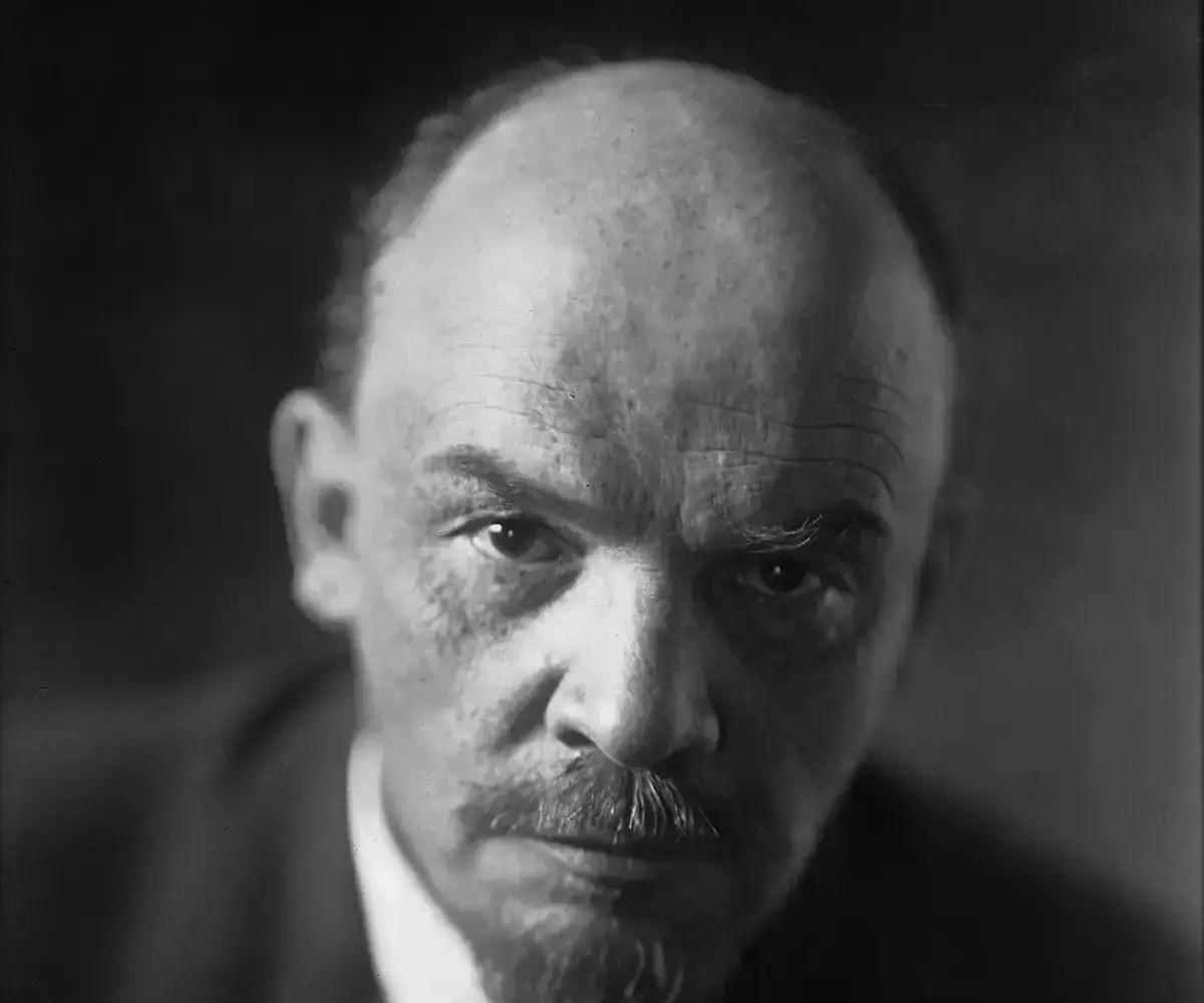 Black-and-white close-up portrait of Vladimir Lenin, bald, with a short beard and moustache, in a dark jacket and tie, looking at the camera
